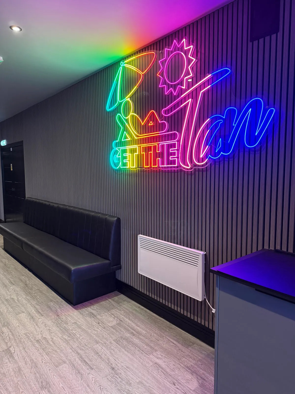 The rainbow "Get The Tan" neon wall and booth seating at Beautano
